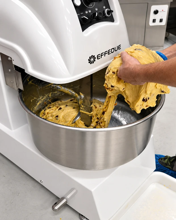 Pâte à panettone soulevée à la main hors de la cuve d'un pétrin à spirale